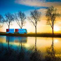 Lorry parked beside a tranquil river at sunset, with silhouetted trees reflecting in the water, showcasing Duncan MacBrayne's commercial photography skills.