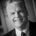 Professional headshot of Peter Webber, smiling in a suit, showcasing Duncan MacBrayne's photography expertise in client portraits.