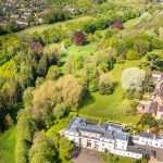 Aerial view of a luxury property surrounded by lush greenery and landscaped gardens, showcasing the expansive grounds and nearby residential area, highlighting Duncan MacBrayne's expertise in commercial property photography.