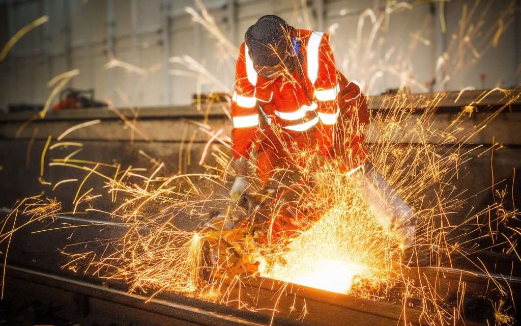 Industrial worker in safety gear cutting metal, creating sparks, showcasing specialist industrial photography for manufacturing and engineering environments.