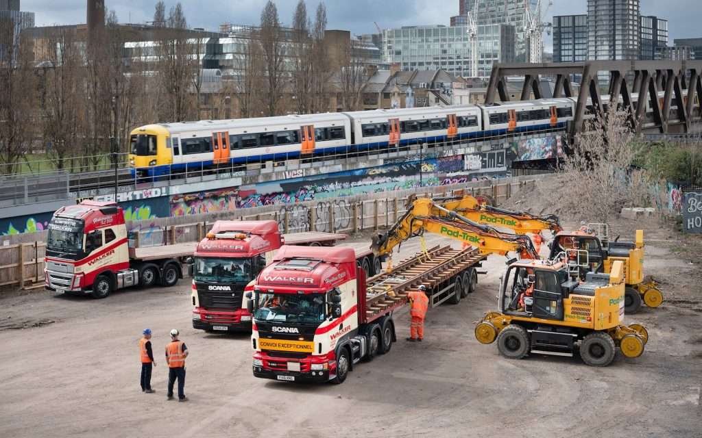 Trucks and construction machinery on an industrial site with railway construction elements, including workers in safety gear, showcasing Duncan MacBrayne's expertise in heavy industry photography.