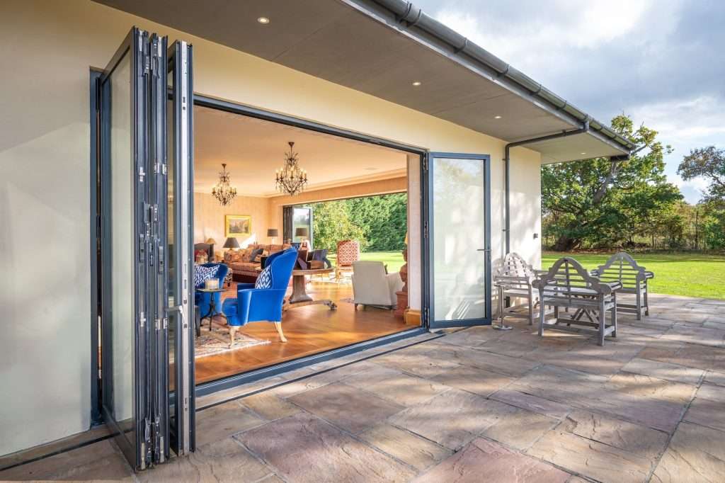 Modern open-plan living space with bifold doors leading to a garden, featuring stylish furniture, chandeliers, and a bright interior, showcasing Duncan MacBrayne's expertise in capturing residential architecture.
