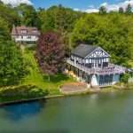 Aerial view of a luxury property by the river, featuring a modern house with a balcony, surrounded by lush greenery, showcasing Duncan MacBrayne's expertise in property photography.