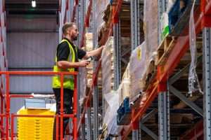 Warehouse worker in high-visibility vest retrieving items from shelves, showcasing industrial photography by Duncan MacBrayne, commercial photographer in Reading, Berkshire.