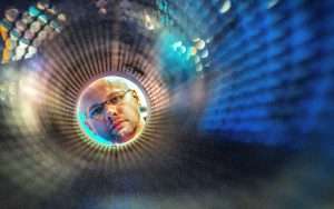 Man looking through a circular aperture, showcasing industrial photography techniques by Duncan MacBrayne, with vibrant colours and textures in the background.