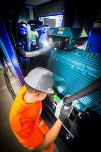 Industrial worker in hard hat and orange shirt operating machinery in commercial setting, showcasing Duncan MacBrayne's industrial photography services.