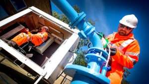 Industrial workers in safety gear operating machinery and monitoring equipment at a construction site, showcasing commercial photography by Duncan MacBrayne.