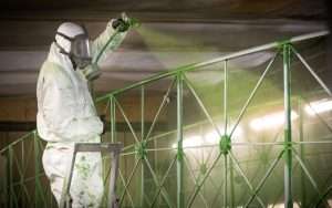 Person in protective gear spray painting a green industrial structure, highlighting Duncan MacBrayne's expertise in industrial photography services.