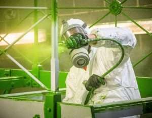 Industrial worker in protective gear applying green paint with spray gun, showcasing commercial photography by Duncan MacBrayne in Reading, Berkshire.