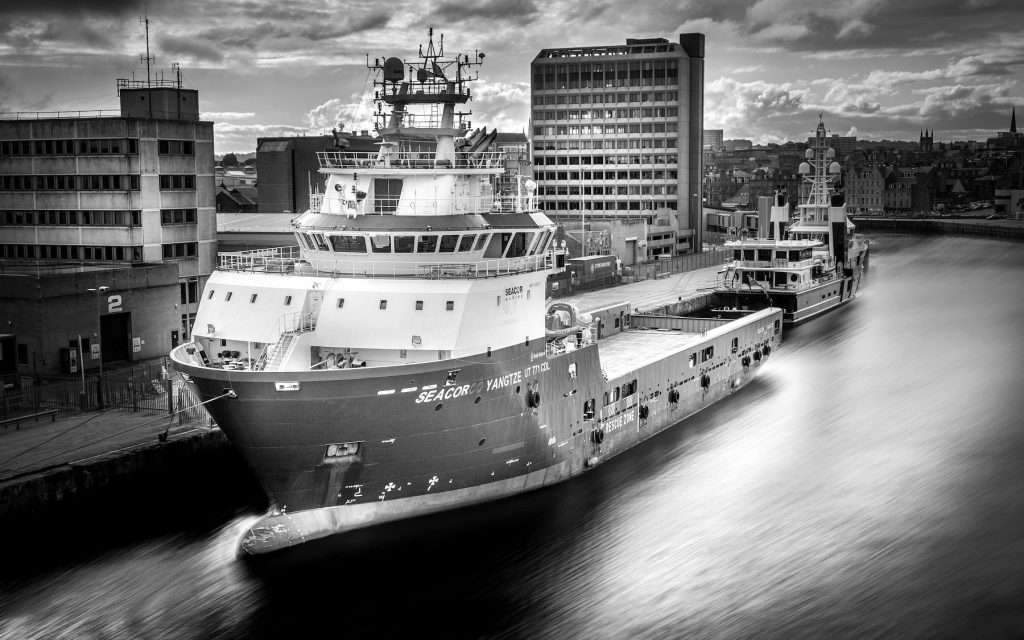 Black and white image of a large industrial ship, the Seacor Yangtze, docked alongside a city waterfront, with modern buildings and a cloudy sky in the background, showcasing industrial and marine photography.
