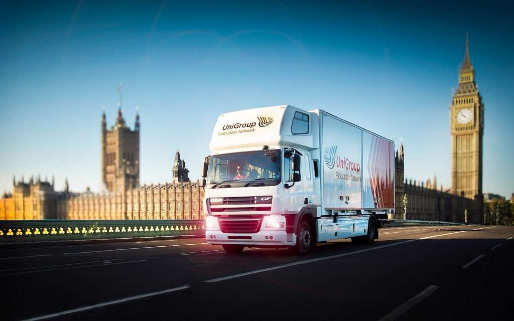 Lorry from UniGroup Relocation Network driving on Westminster Bridge with the iconic Big Ben in the background, showcasing commercial transportation in an urban setting.