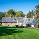 Luxury property with stone exterior and slate roof, set in lush green surroundings, showcasing residential architecture.