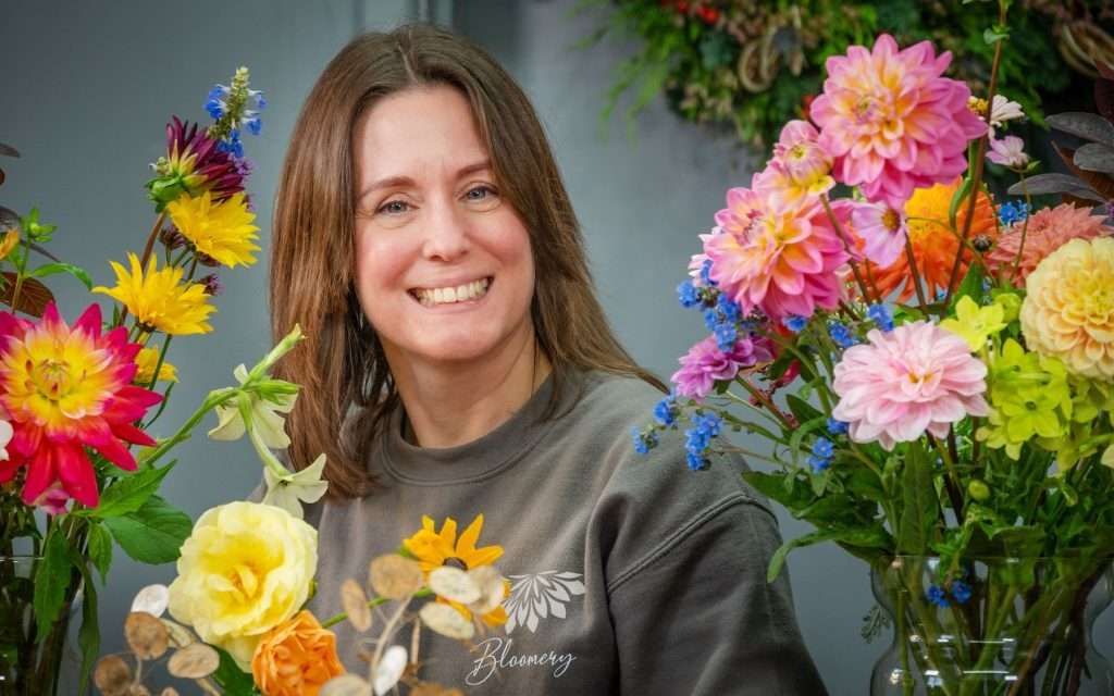 Woman smiling among vibrant flowers, showcasing floral arrangements for commercial photography, highlighting Duncan MacBrayne's services in Reading, Berkshire.