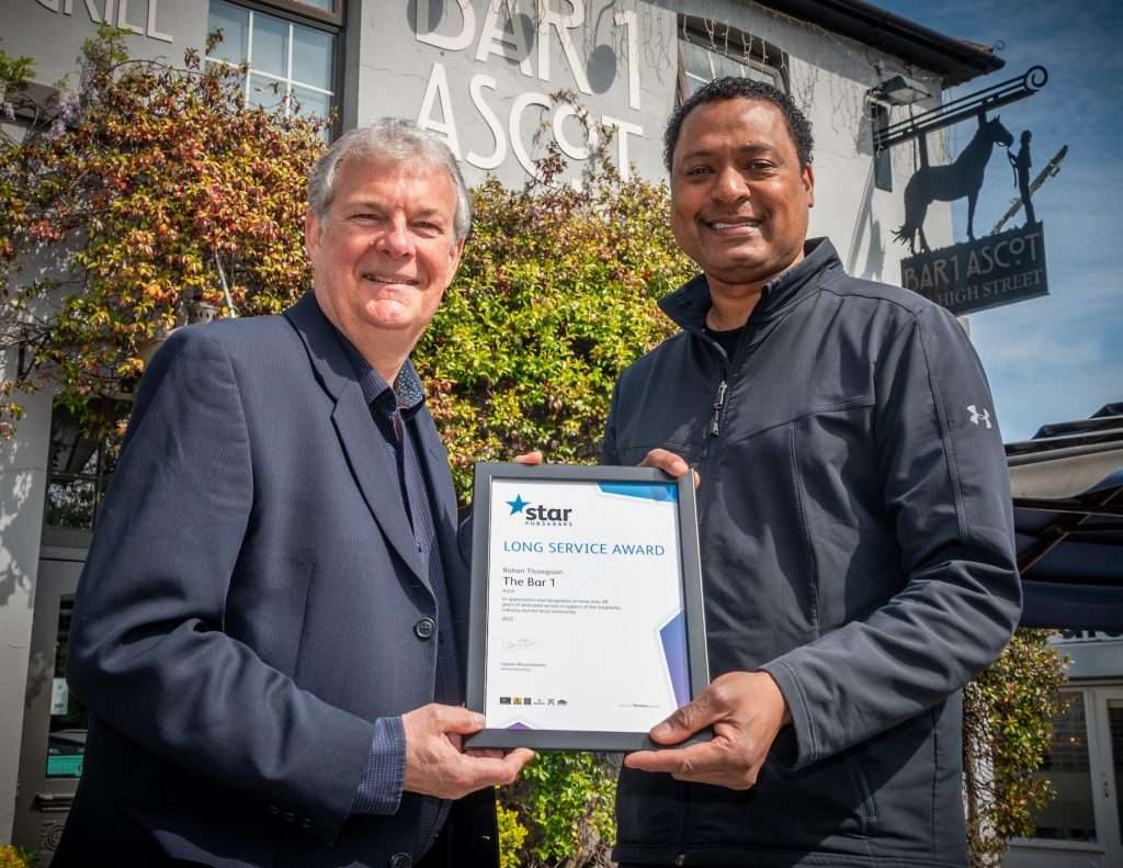 Two men holding a Long Service Award certificate outside The Bar 1 in Ascot, showcasing a professional photography scene.
