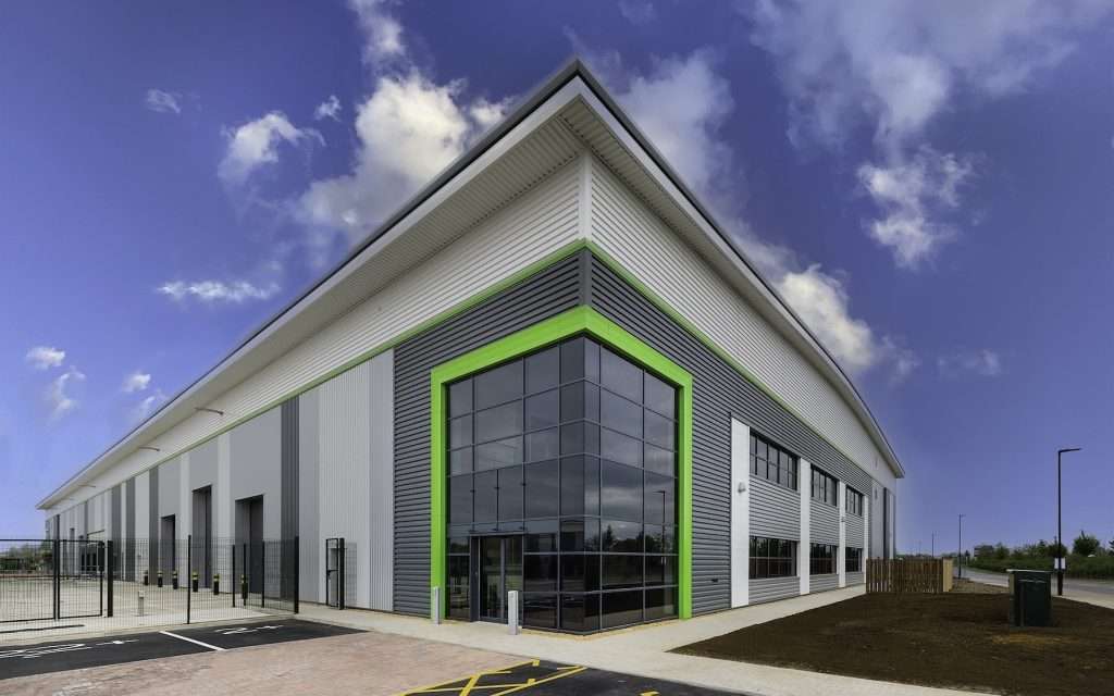 Modern industrial building exterior in Reading, featuring large glass windows, green accents, and a clear blue sky, showcasing Duncan MacBrayne's commercial photography services.