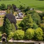 Aerial view of a modern luxury property surrounded by lush greenery and trees, showcasing landscaped gardens and nearby fields, highlighting Duncan MacBrayne's expertise in commercial property photography in Berkshire.