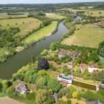 Aerial view of lush countryside with a river, residential properties, and greenery, showcasing the scenic landscape of Reading and Berkshire, relevant to commercial property photography.