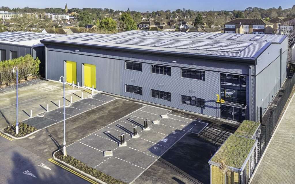 Aerial view of a modern industrial building with yellow doors, surrounded by a parking lot and greenery, showcasing commercial property for marketing and investment purposes.