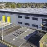 Industrial building exterior with grey cladding, yellow doors, and a spacious parking area, showcasing commercial property photography by Duncan MacBrayne in Reading, Berkshire.