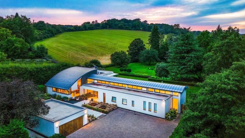 Modern luxury property in a rural setting, featuring sleek architecture, expansive gardens, and a backdrop of rolling hills and trees at sunset.