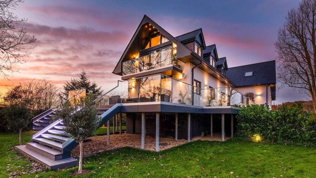 Modern luxury property with illuminated staircase and glass balcony at sunset, showcasing architectural design and landscaping in Reading, Berkshire.