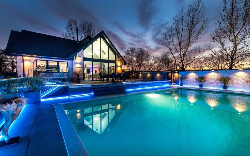 Luxury home with illuminated swimming pool and modern architecture at dusk, showcasing professional property photography by Duncan MacBrayne in Berkshire.
