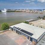 Aerial view of an industrial building with solar panels, overlooking a river and city skyline, showcasing commercial property photography by Duncan MacBrayne in Reading, Berkshire.