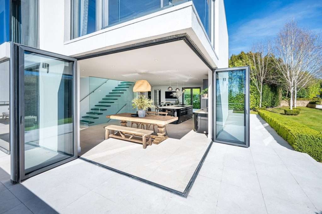 High-end residential property showcasing modern interior design, open-plan layout with dining area, large windows, and landscaped garden visible outside.