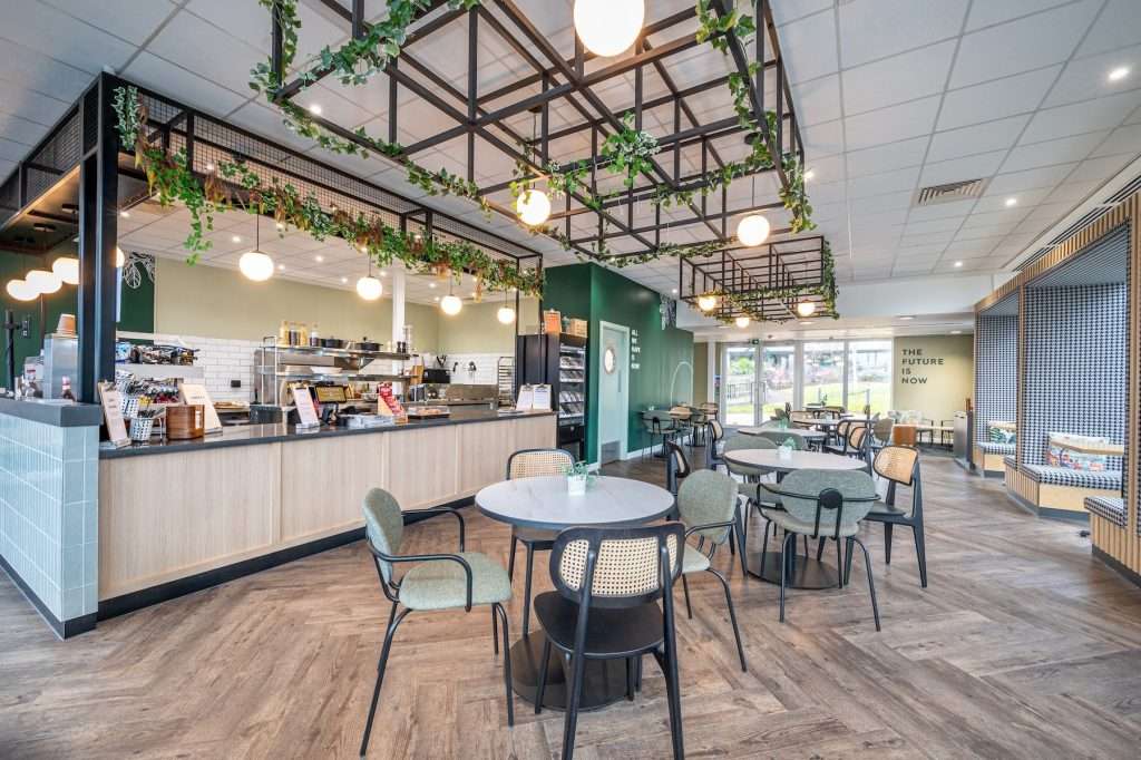Modern café interior with a wooden counter, seating areas, pendant lights, and greenery, showcasing a welcoming atmosphere for customers in Reading, Berkshire.