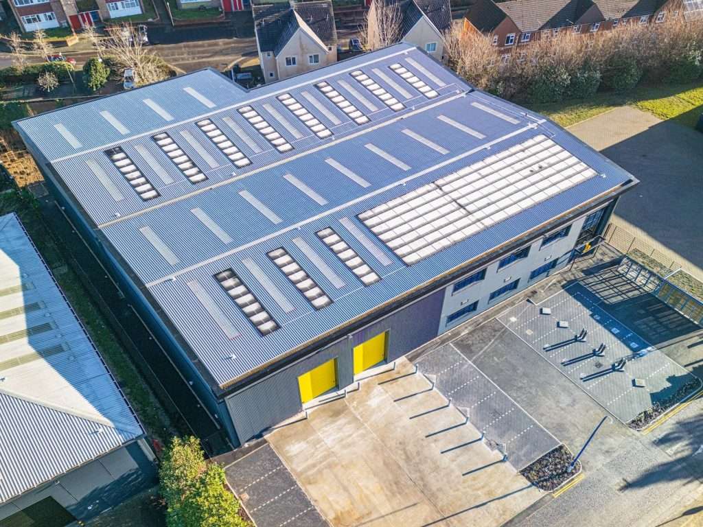 Aerial view of a modern industrial building with a flat roof featuring skylights and yellow doors, surrounded by a paved area and residential properties, showcasing commercial architecture in Reading, Berkshire.