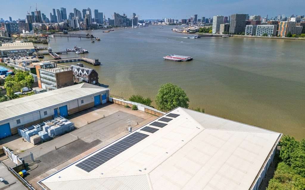 Aerial view of industrial buildings along the river, featuring solar panels on the roof and a boat navigating the water, showcasing the urban landscape of Reading, Berkshire.