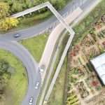 Aerial view of a roundabout with vehicles navigating, surrounded by greenery and a garden centre, showcasing industrial and commercial infrastructure.