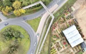 Aerial view of a roundabout with vehicles, surrounded by greenery and a garden centre featuring a greenhouse and landscaped areas.