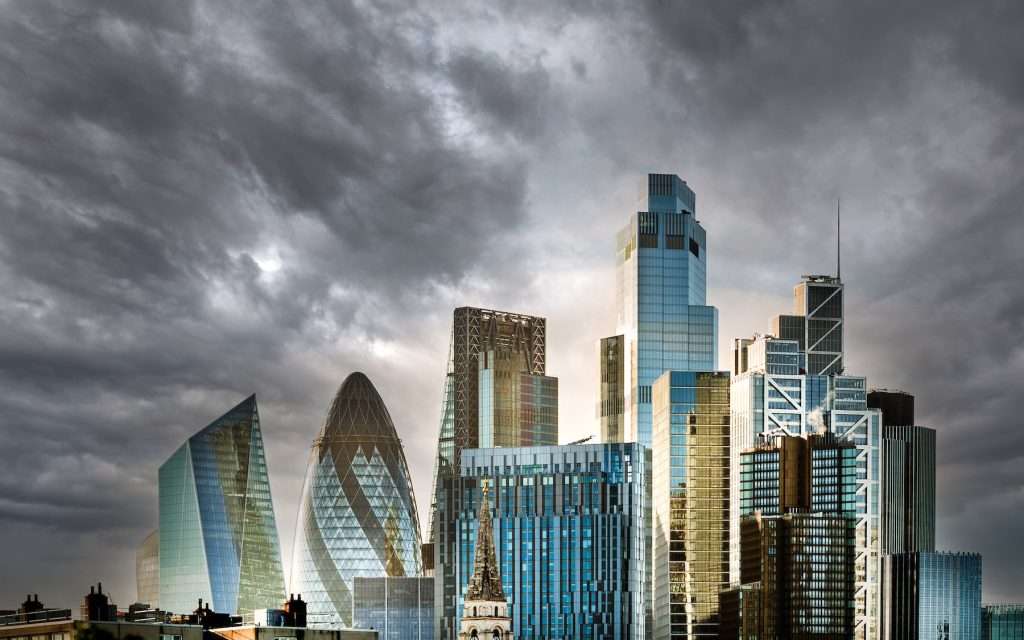 City skyline featuring modern architectural designs with glass facades under a dramatic cloudy sky, representing commercial and industrial photography by Duncan MacBrayne in Reading, Berkshire.