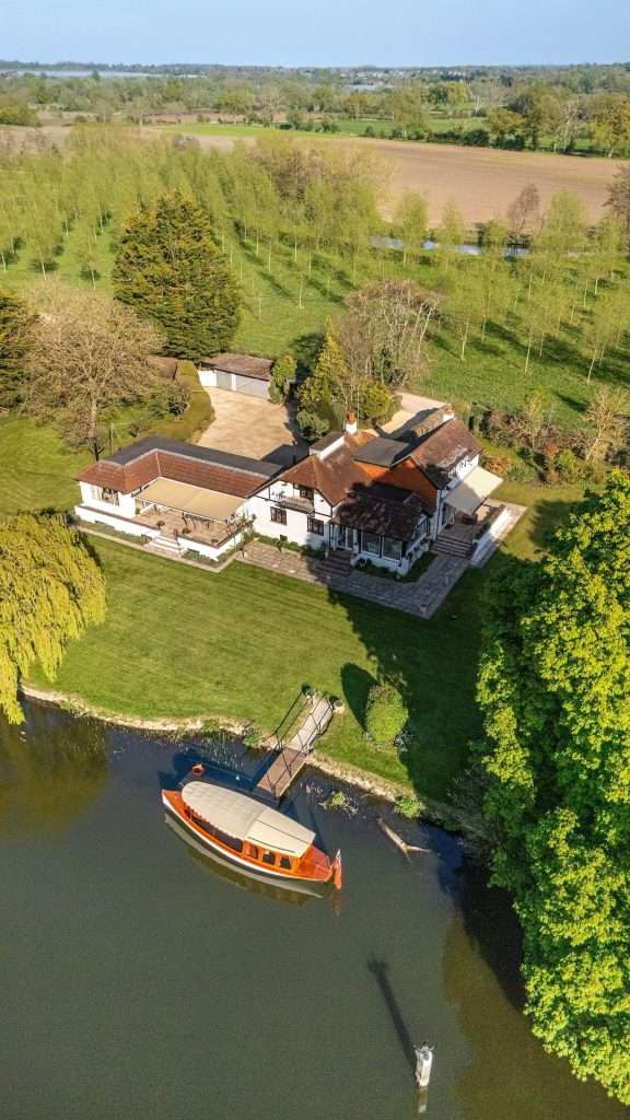 Aerial view of a luxury property with landscaped garden, featuring a moored boat on the water, set in a serene rural environment in Berkshire.