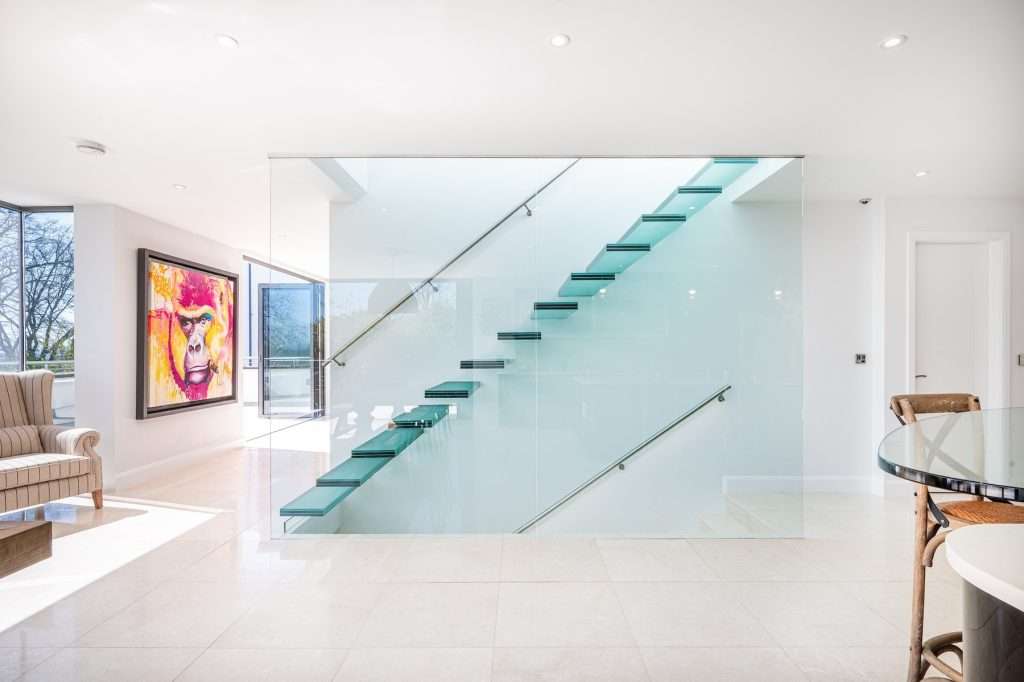 Modern interior featuring a glass staircase, contemporary art piece, and stylish furniture, showcasing luxury property photography by Duncan MacBrayne.