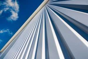 Close-up of architectural metal cladding with vertical lines against a blue sky, showcasing industrial design elements relevant to Duncan MacBrayne's commercial photography services in Reading, Berkshire.