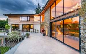Modern residential property with large glass windows and wooden exterior, showcasing architectural design and outdoor patio, reflecting Duncan MacBrayne's expertise in property photography.