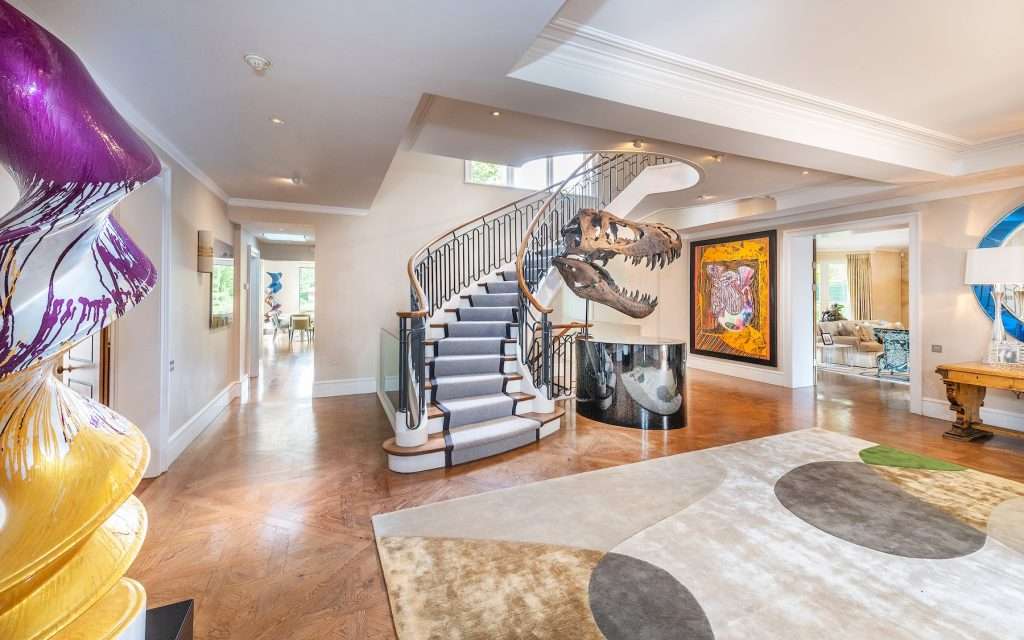 Interior hallway featuring a striking spiral staircase, dinosaur skull sculpture, colourful abstract artwork, and designer rugs, showcasing luxurious property aesthetics for interior design photography.