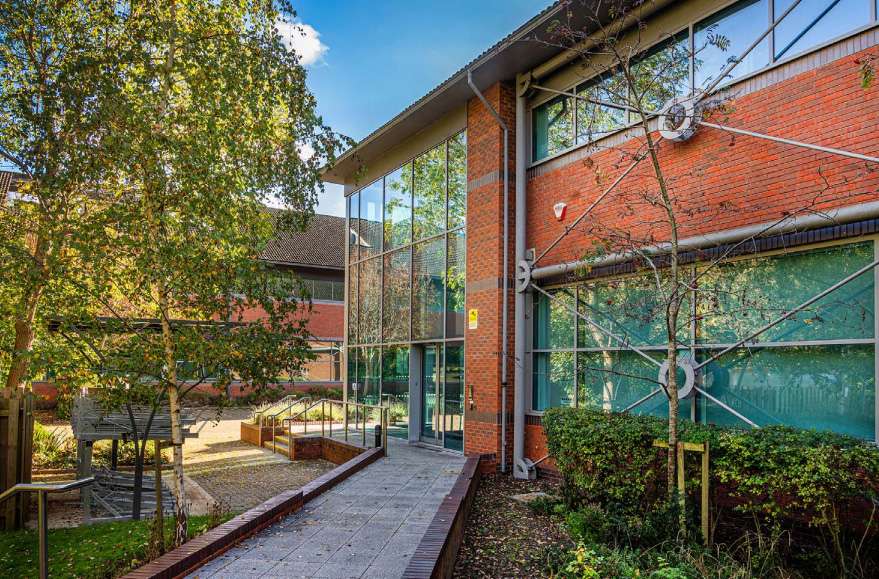 Modern office building entrance with large glass windows, brick façade, landscaped pathway, and surrounding greenery, showcasing commercial property photography by Duncan MacBrayne.